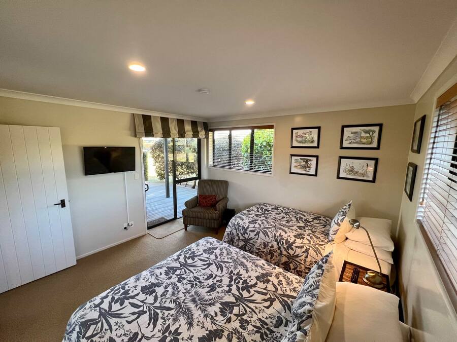 A bedroom with a bed, a chair, a TV, and a window with blinds.