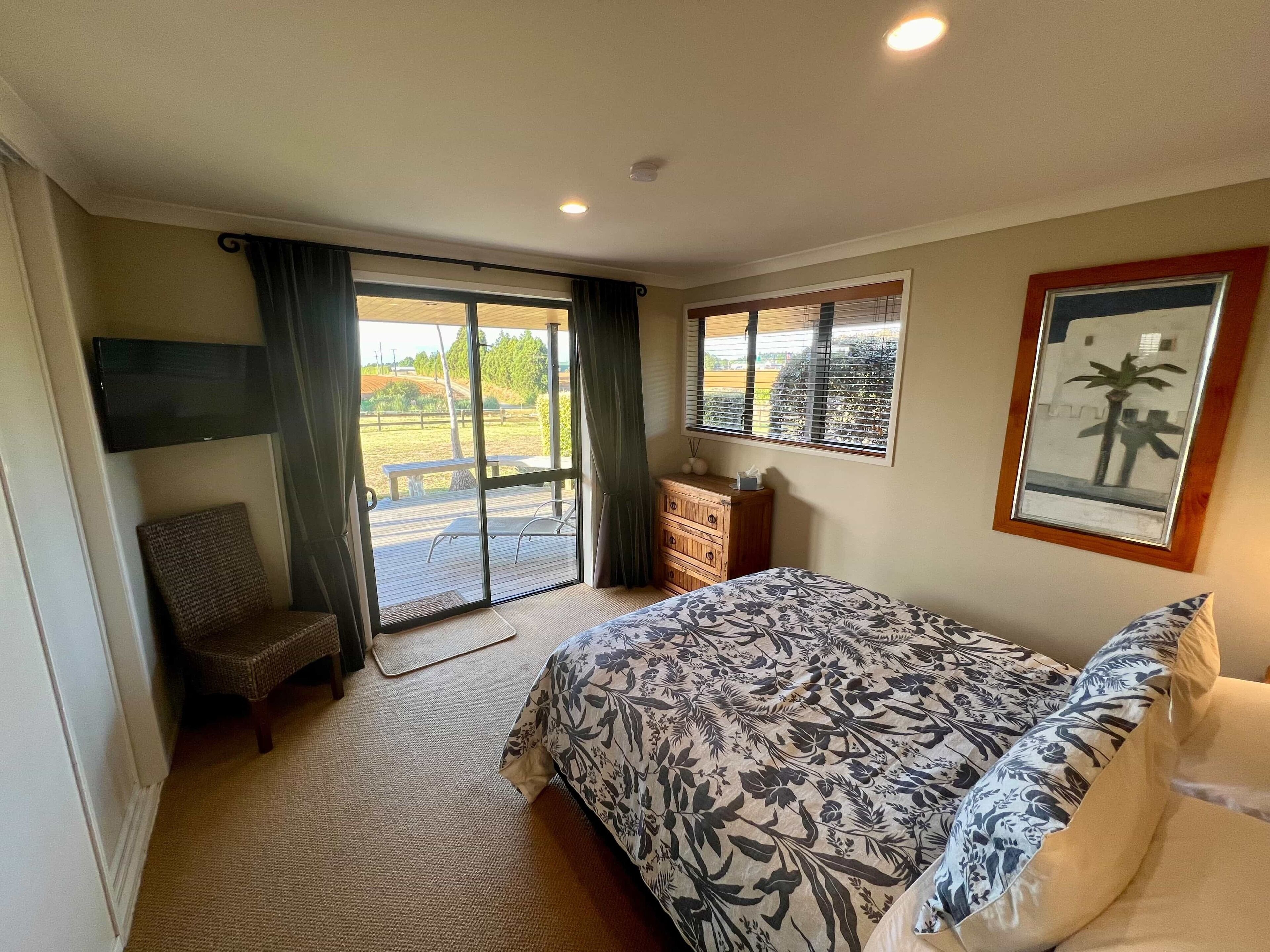 Een slaapkamer met een groot bed, een stoel, een kaptafel en een schuifdeur naar een buitenruimte.