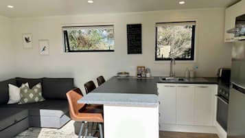 A modern kitchen with a central island, white cabinets, and a dining area with a grey sofa and brown chairs.