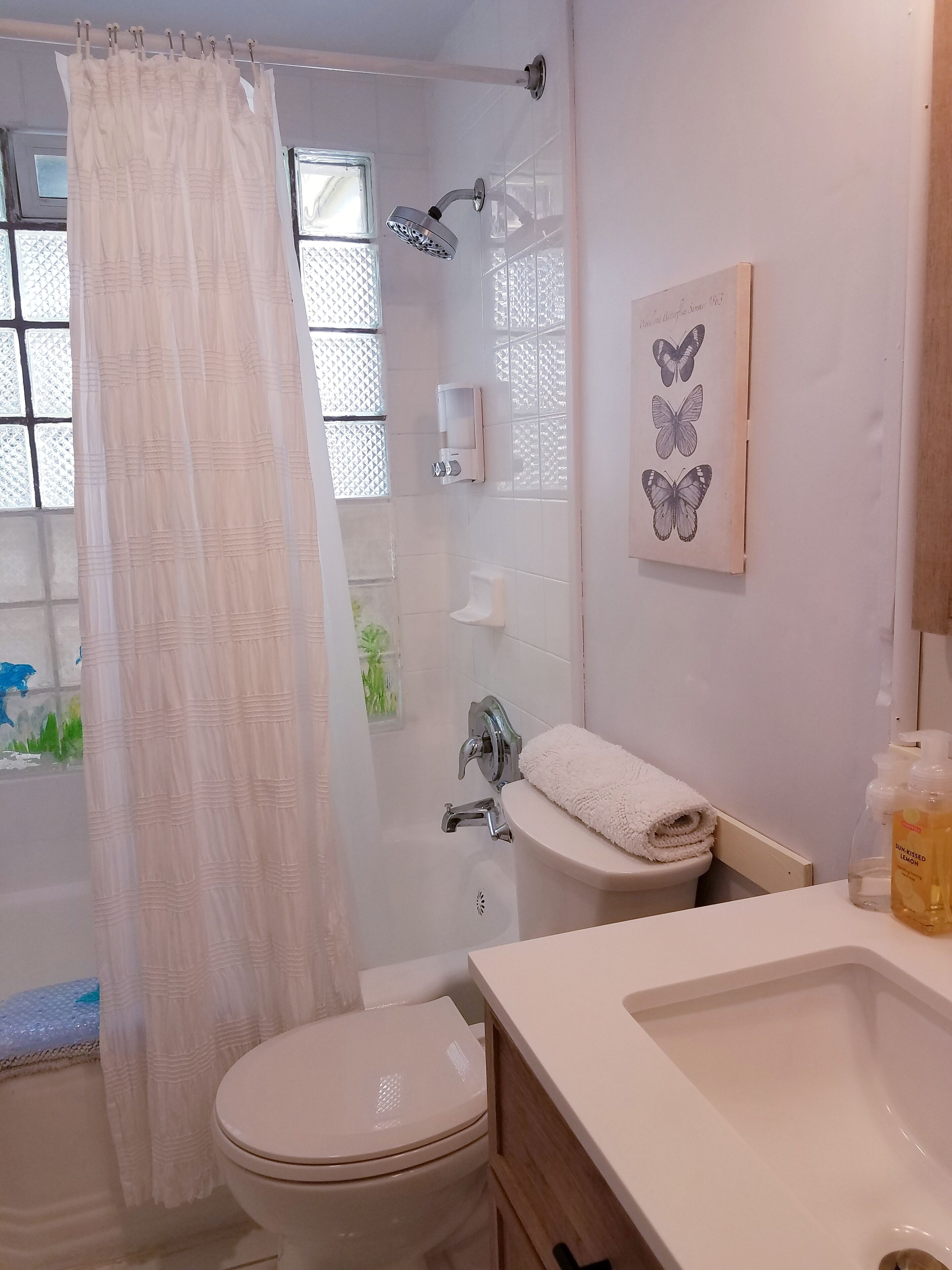 A bathroom with a shower, toilet, sink, and a window with a curtain.