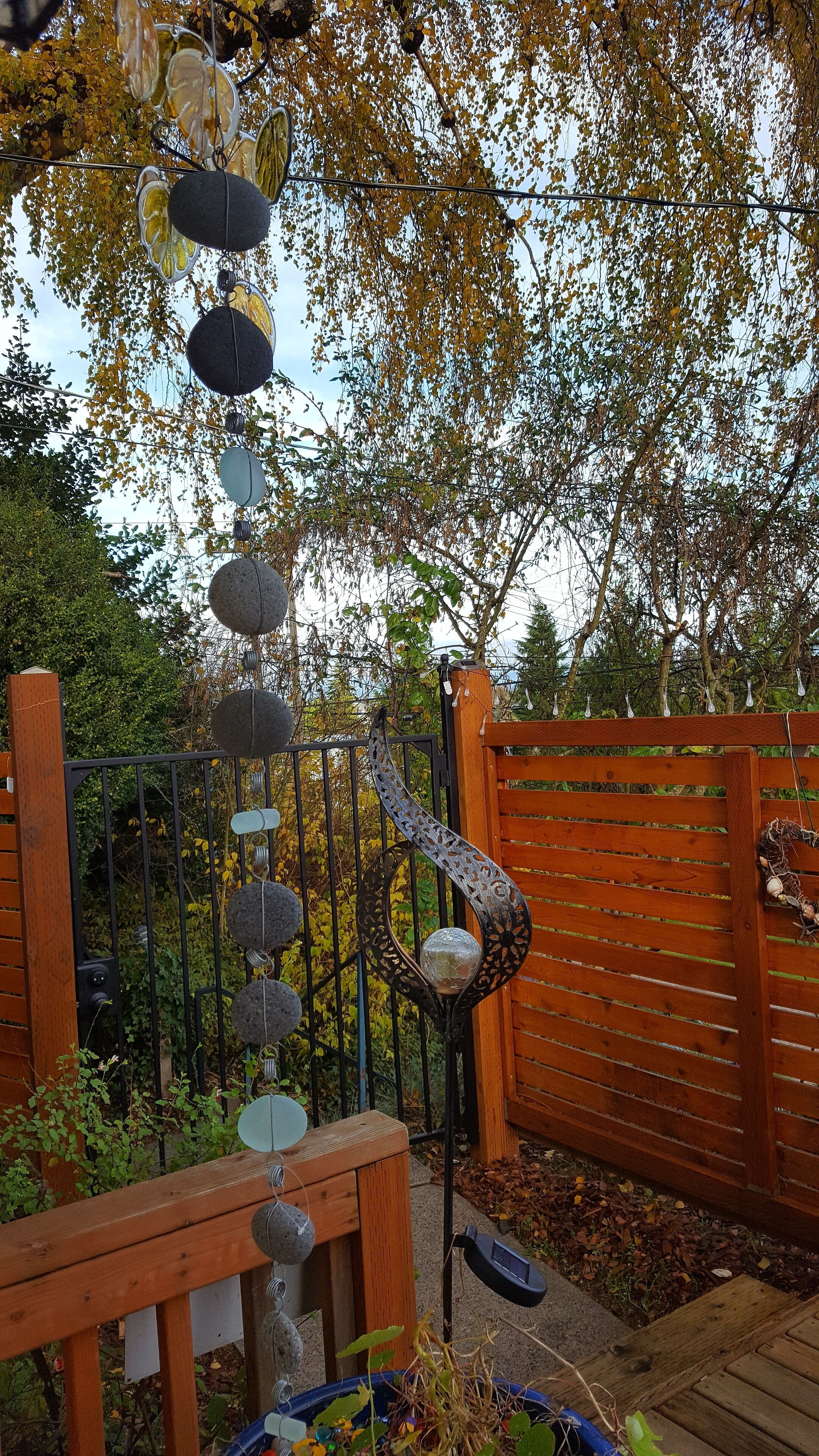 A garden with a wooden fence, a metal gate, and a decorative hanging structure with stones and glass elements.
