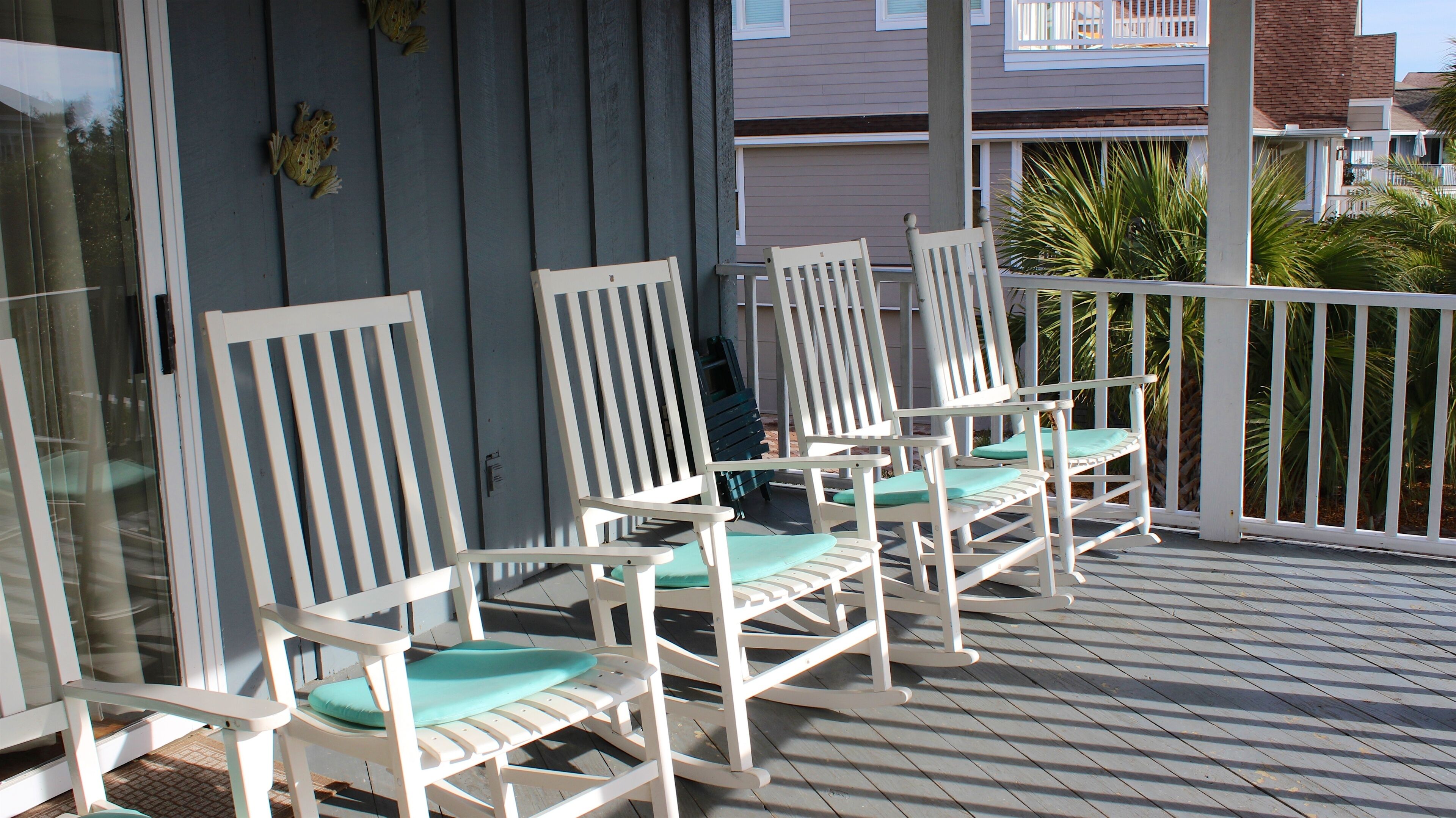 A wooden deck with white rocking chairs and a white railing.