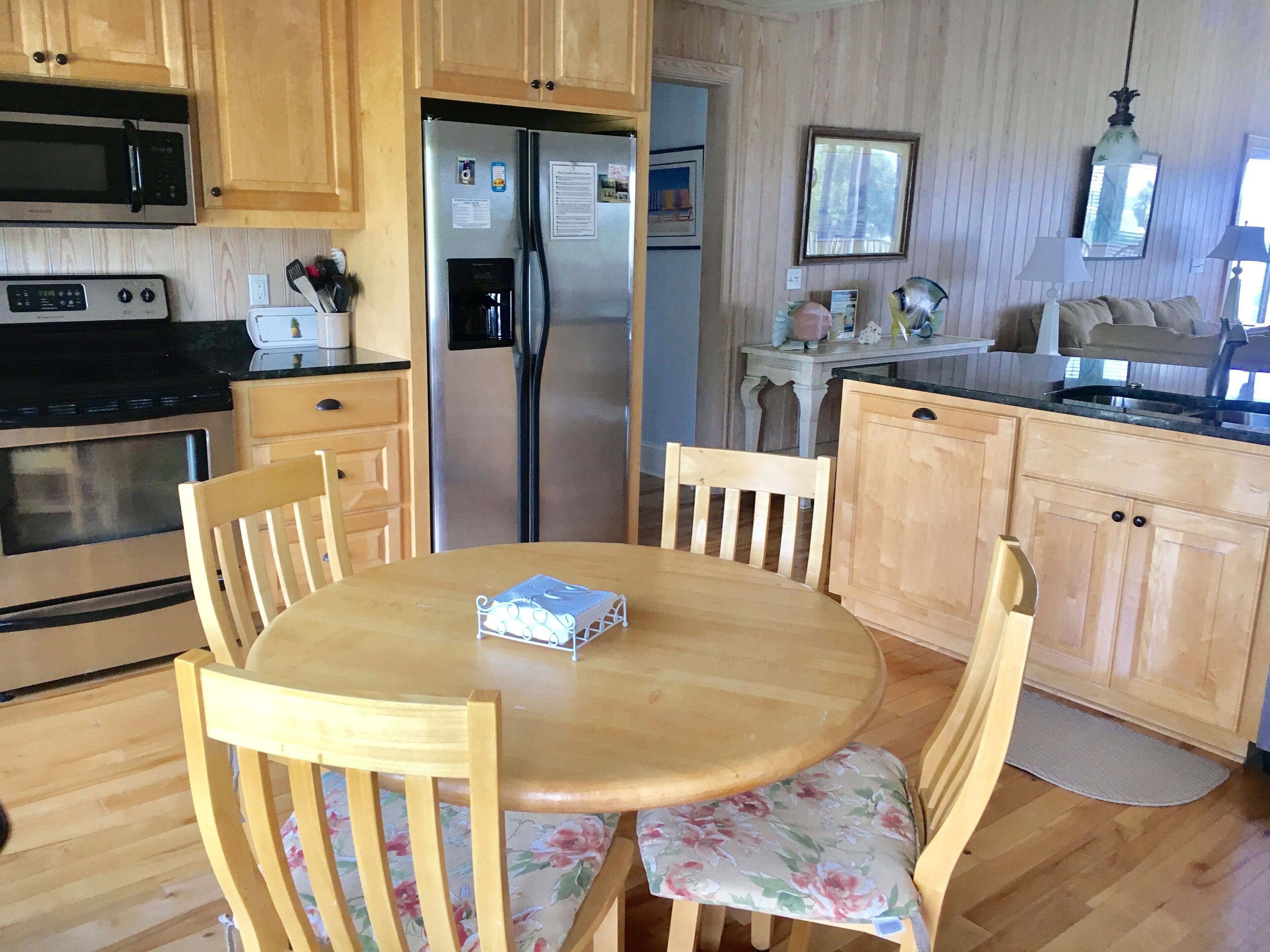 A kitchen with wooden cabinets, a stainless steel refrigerator, a microwave, and a dining table with floral chairs.