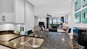 Una cocina moderna con encimera de granito, pileta de acero inoxidable y una cafetera Keurig.