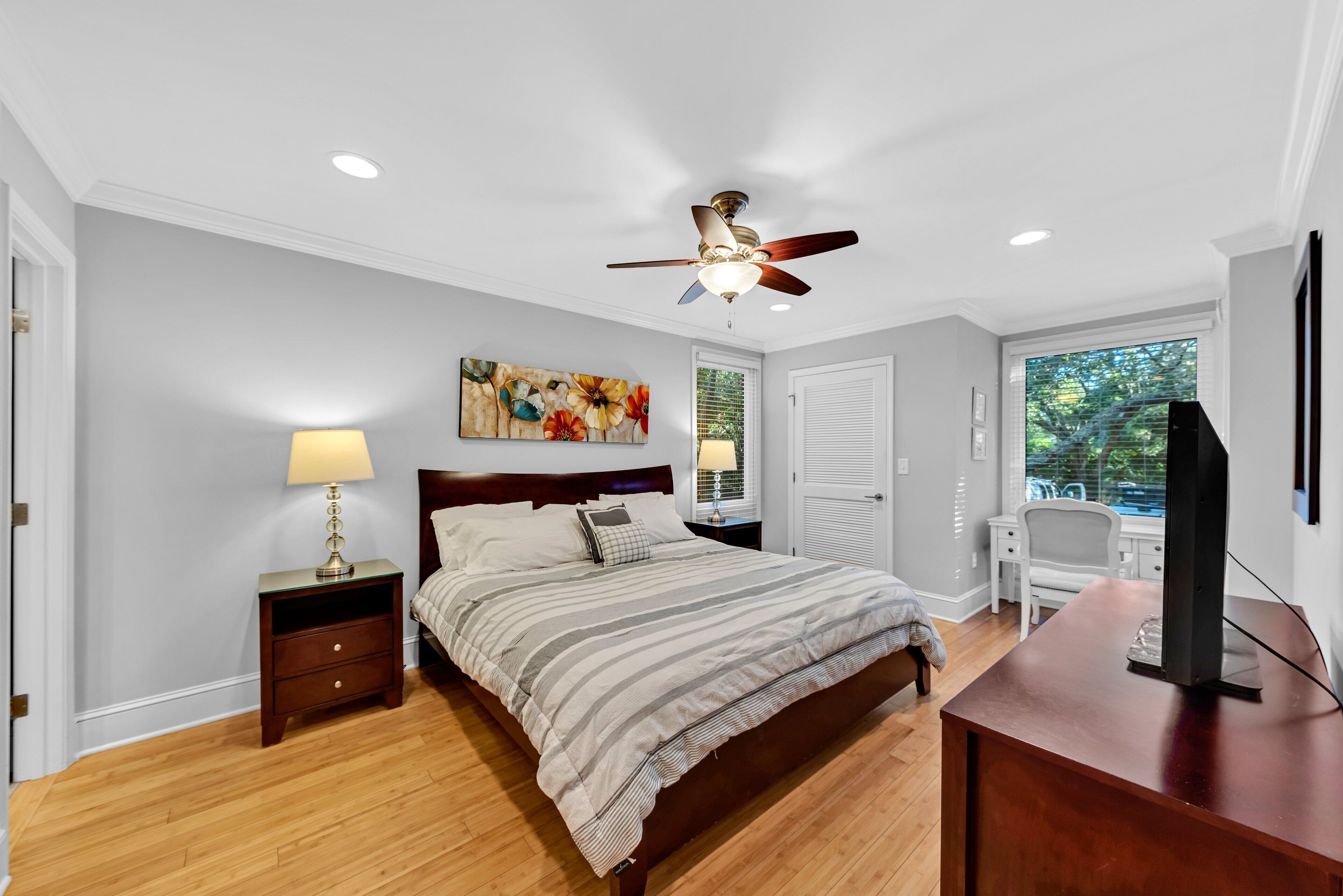 A bedroom with a bed, nightstands, a desk, a ceiling fan, and a window with blinds.