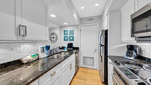 Una cocina moderna con armarios blancos, encimera de granito, electrodomésticos de acero inoxidable y suelo de madera.