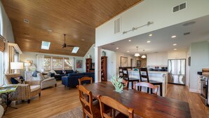 A spacious living area with a wooden dining table, chairs, and a sofa. A kitchen with modern appliances is visible in the background.