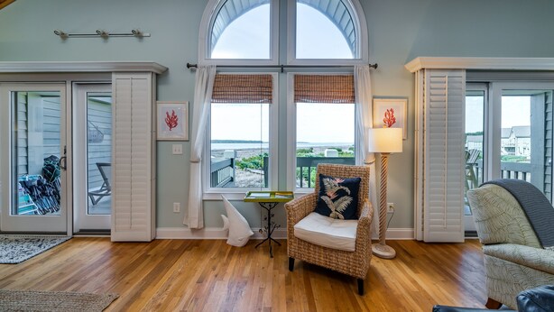 A spacious room with a large arched window, a wicker chair with a cushion, a small table, and a lamp.