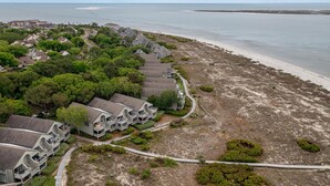 An aerial view of a coastal hotel with multiple-story buildings, a beachfront, and a well-maintained garden area.