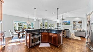 Une cuisine moderne dotée d’un îlot central, de meubles en bois, d’appareils électroménagers en acier inoxydable et de luminaires suspendus.