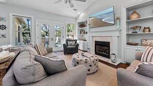 Un salon spacieux avec un grand canapé, une cheminée et un téléviseur diffusant une scène de plage.