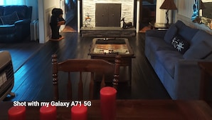 A cozy living room with a fireplace, wooden beams, and a blue sofa. - Lake front property with one dock space for boat/jet ski on Lake Wallenpaupack. (Greentown)