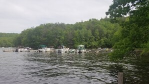 A calm lake with several boats docked at a pier, surrounded by dense green trees. - Lake front property with one dock space for boat/jet ski on Lake Wallenpaupack. (Greentown)