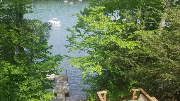 A wooden deck with outdoor seating overlooking a lake surrounded by trees. - Lake front property with one dock space for boat/jet ski on Lake Wallenpaupack. (Greentown)