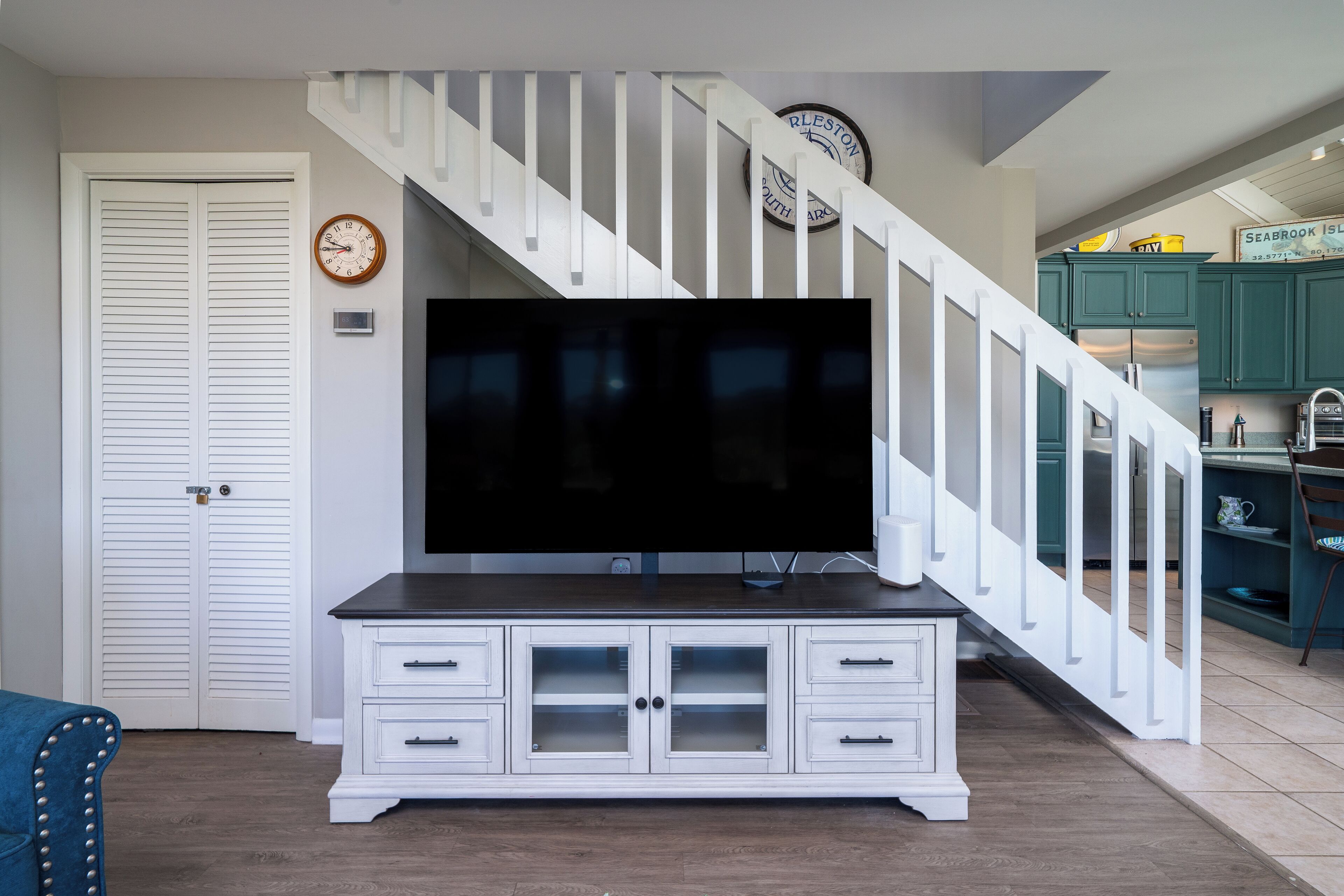 A living room with a white entertainment center, a flat-screen TV, and a staircase with white railings.