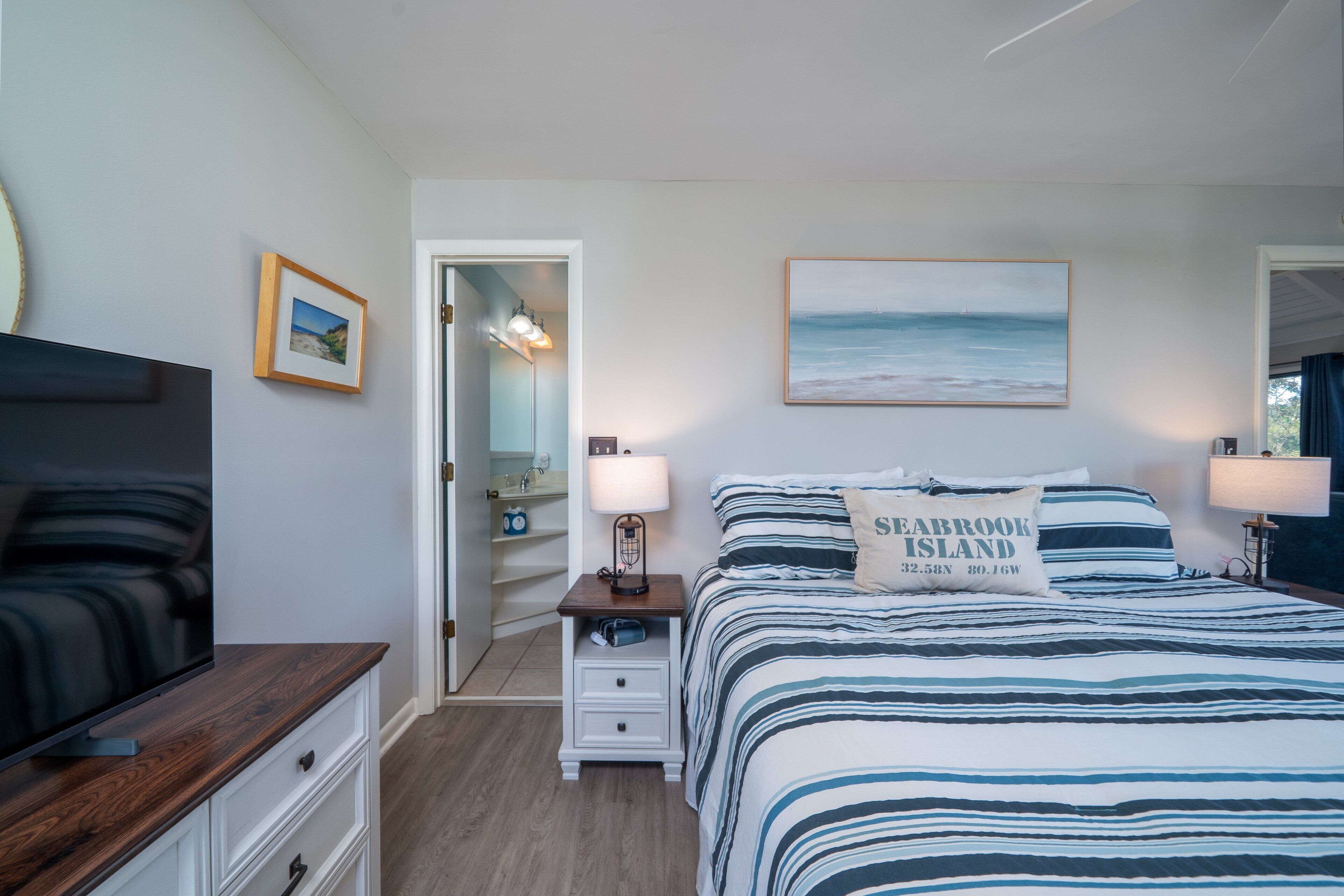 Une chambre à coucher avec un lit, des tables de chevet, une télévision et un tableau représentant une plage.