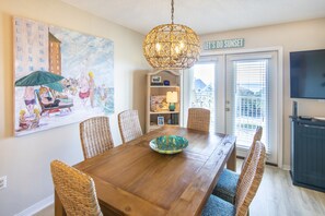 A dining area with a wooden table, wicker chairs, a decorative bowl, and a hanging light fixture.