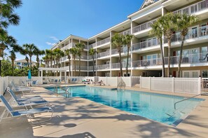 A hotel with a swimming pool, multiple balconies, and palm trees.
