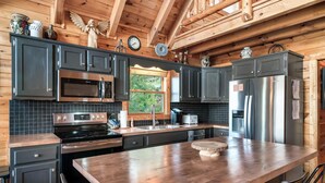A modern kitchen with dark cabinets, stainless steel appliances, and a large wooden island. - Best Panoramic Views! Hot Tub | Fire Pit | Top 10% (Sevierville)