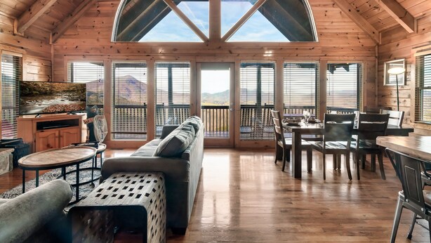 A spacious wooden cabin with a high ceiling, large windows, a cozy seating area, and a dining table. - Best Panoramic Views! Hot Tub | Fire Pit | Top 10% (Sevierville)