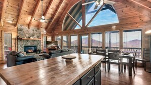 A spacious living area with a stone fireplace, wooden ceiling, and large windows offering mountain views. - Best Panoramic Views! Hot Tub | Fire Pit | Top 10% (Sevierville)