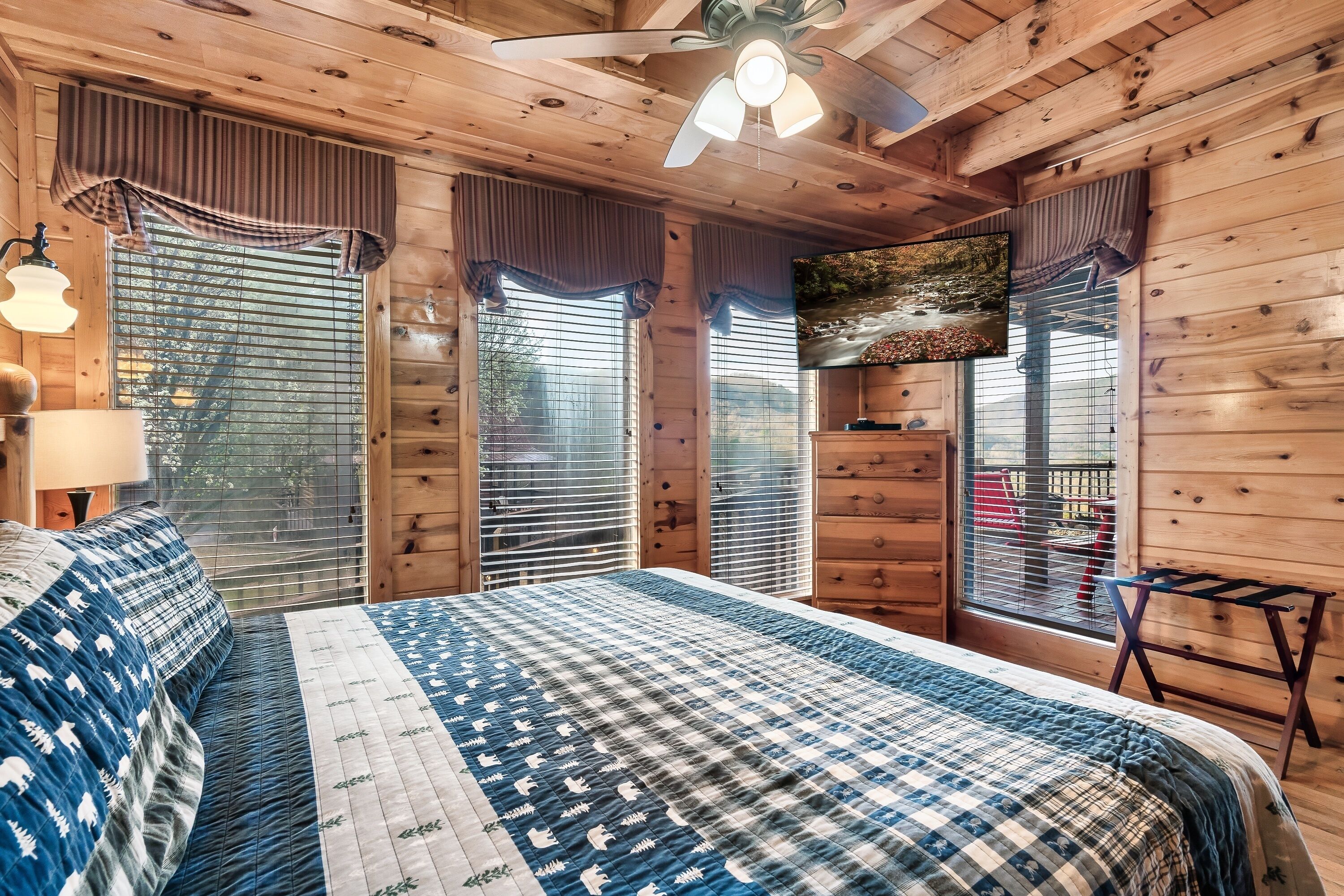 A wooden cabin bedroom with a large bed, a ceiling fan, and a TV mounted on the wall.