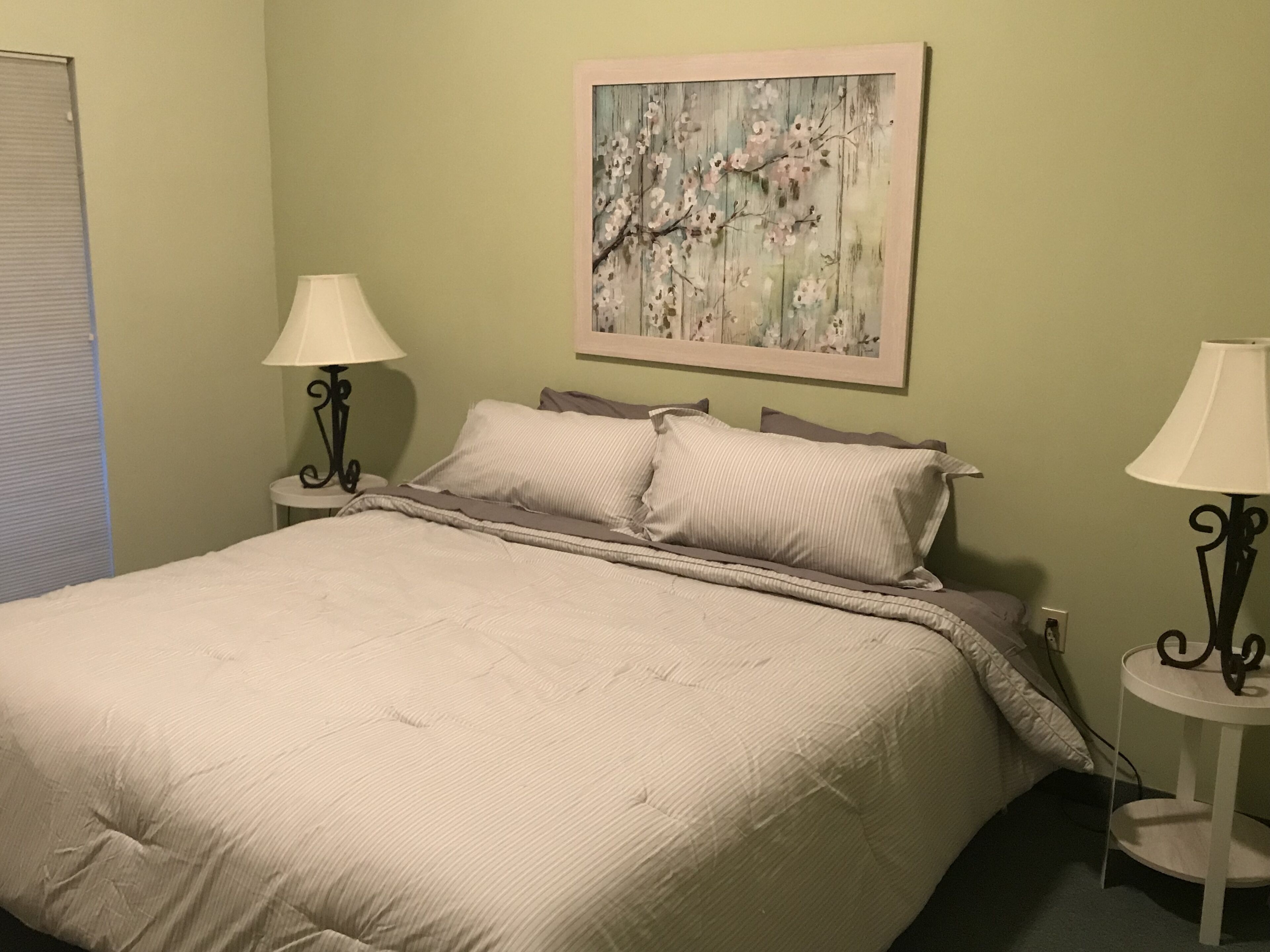 Un lit bien fait, recouvert d’une courtepointe matelassée et agrémenté de deux oreillers, flanqué de deux tables de chevet avec des lampes, dans une pièce aux murs vert clair.