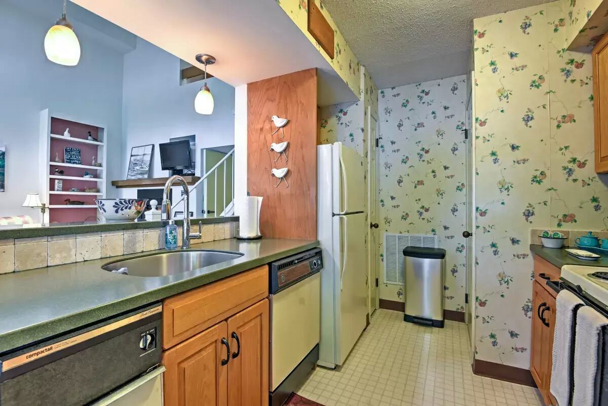 A compact kitchen with a sink, dishwasher, refrigerator, and wooden cabinets.
