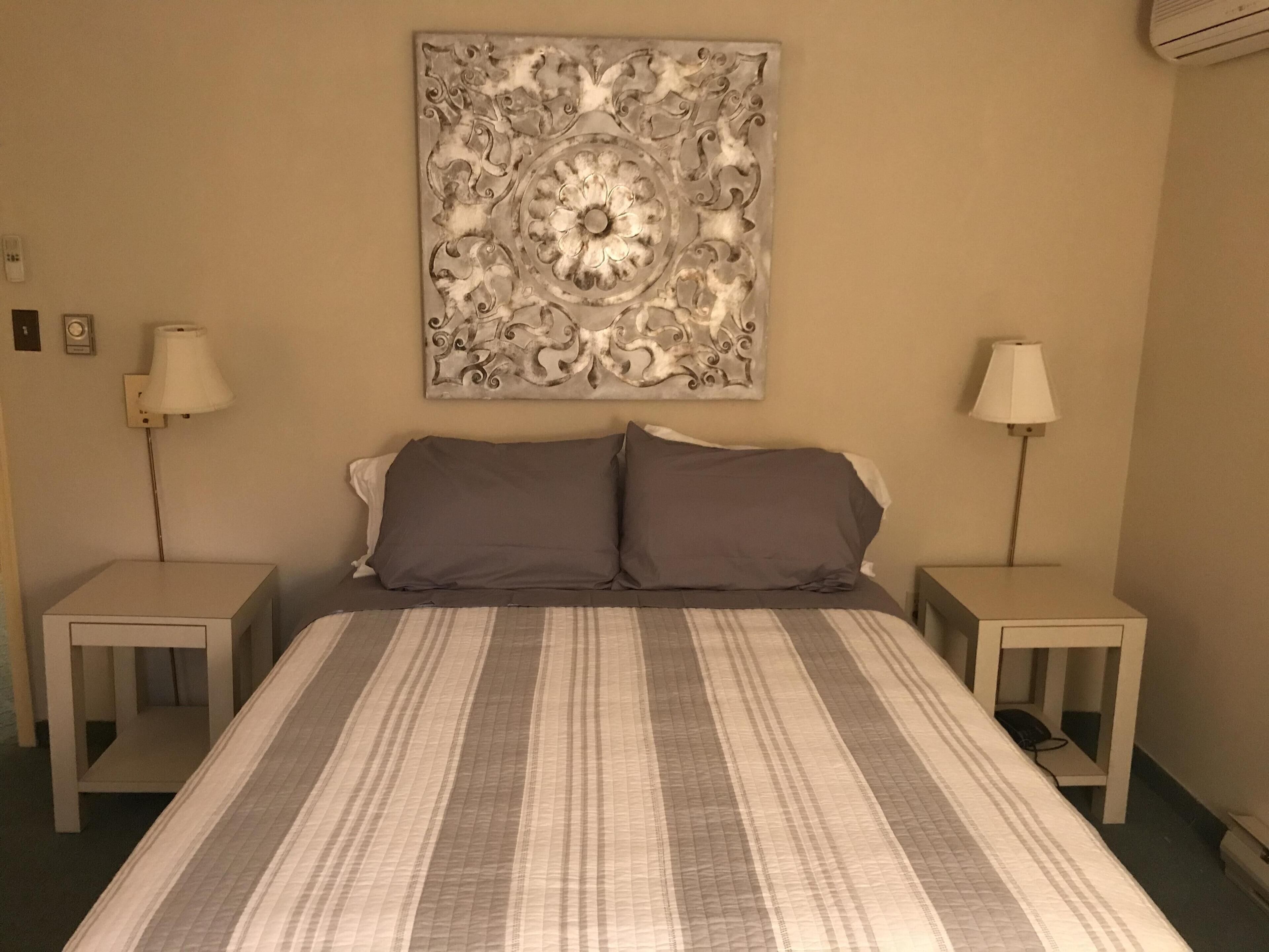 A hotel room with a large bed, two bedside tables, two lamps, and a decorative wall piece above the bed.