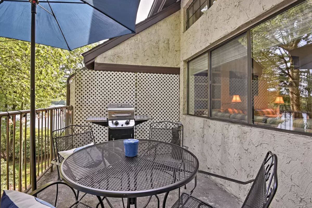 An outdoor patio with a round metal table, chairs, a grill, and a large umbrella.
