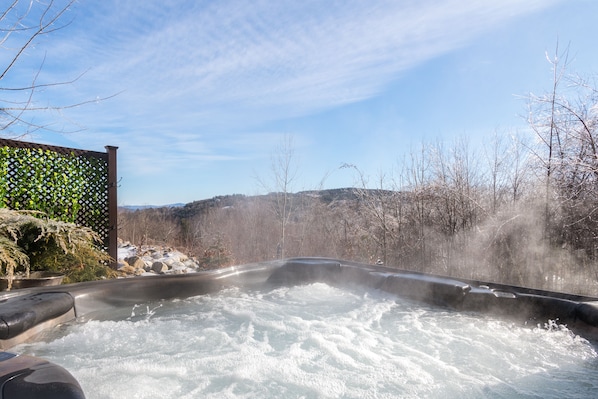 A hot tub with a view of a snowy landscape and bare trees.