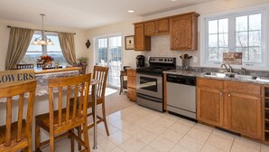 A kitchen with wooden cabinets, a stove, and a dishwasher. There is a window with a view of trees and a sign that says "Apples."