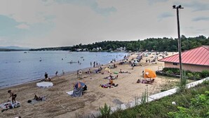 A beach with tents and umbrellas, a lifeguard tower, and a building with a red roof.