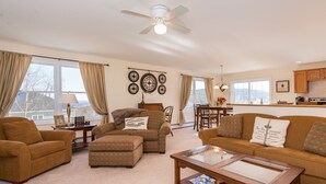 A spacious living room with a ceiling fan, a dining area with a chandelier, and a kitchen with wooden cabinets.