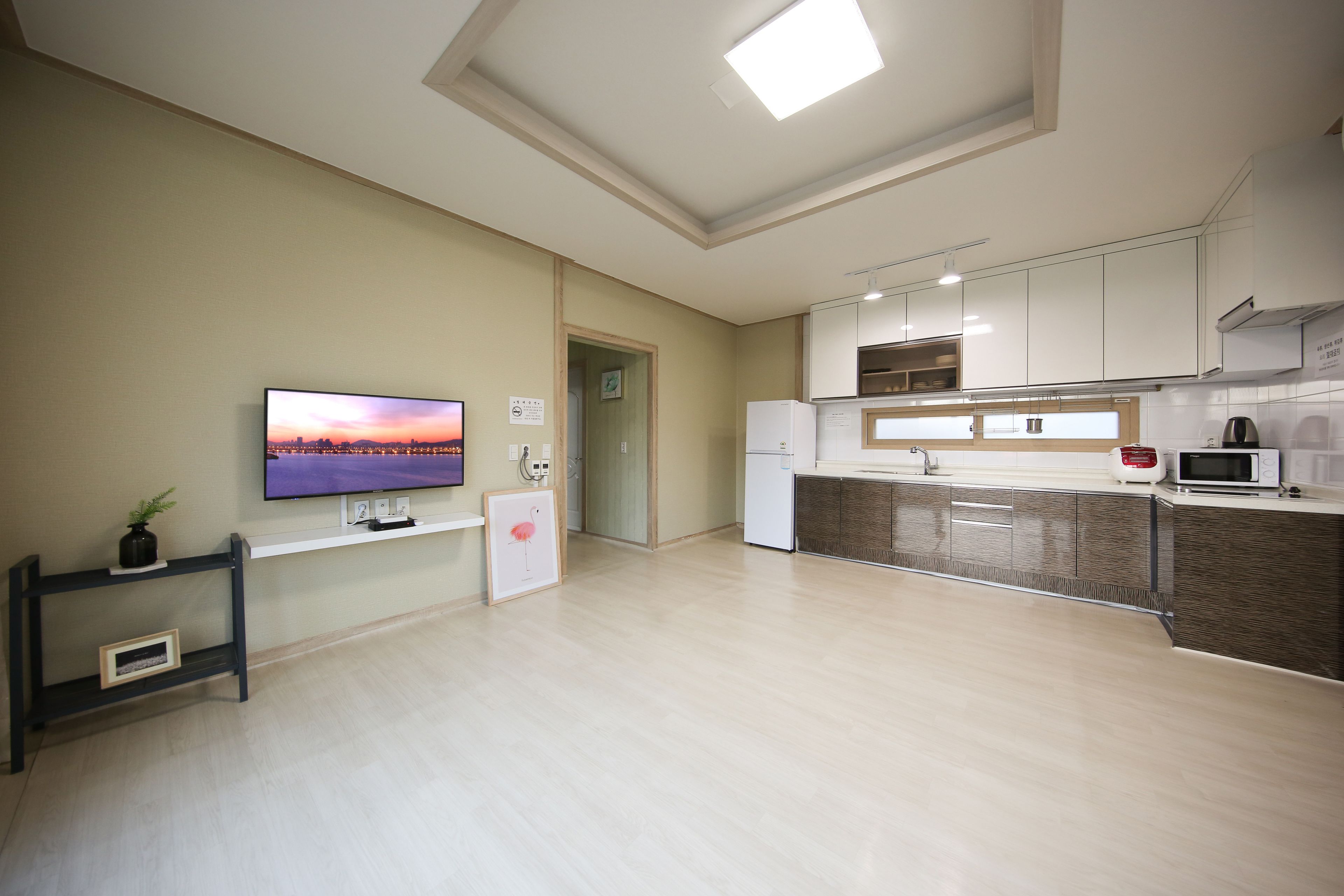 A modern kitchen with a flat-screen TV, white cabinets, and a microwave.