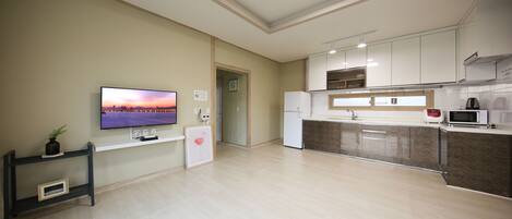 A modern kitchen with a flat-screen TV, white cabinets, and a microwave.