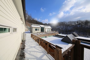 A wooden deck with snow-covered railings and a view of a house with a green door and windows.