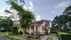 A two-story house with a tiled roof, a front yard with a lawn and a small garden, and a paved driveway. - Villa Sasky Ciater Highland (Ciater)