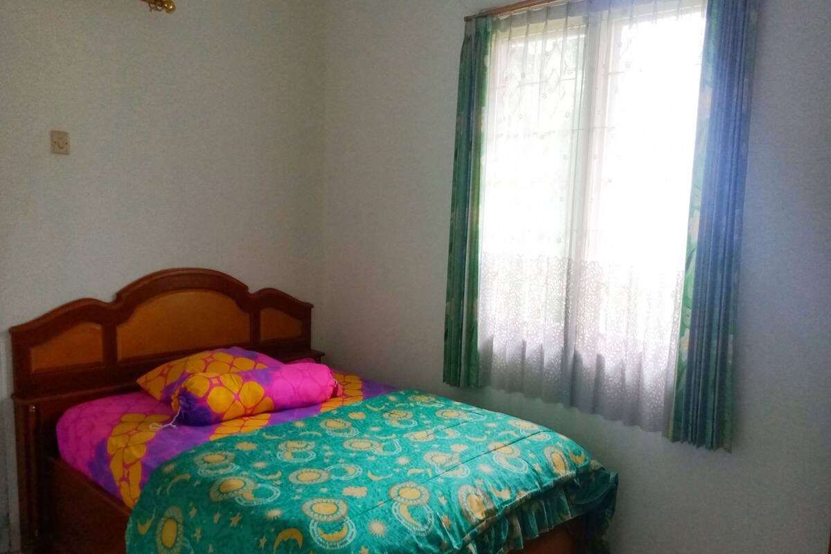 Une chambre à coucher avec un lit en bois, une literie aux couleurs vives, une fenêtre avec des rideaux et un sol carrelé.