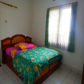 A bedroom with a wooden bed, colorful bedding, a window with curtains, and a tiled floor.