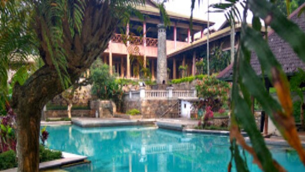 A pool area with a clear view of the pool, surrounding greenery, and a building with a balcony. - Villa Sasky Ciater Highland (Ciater)