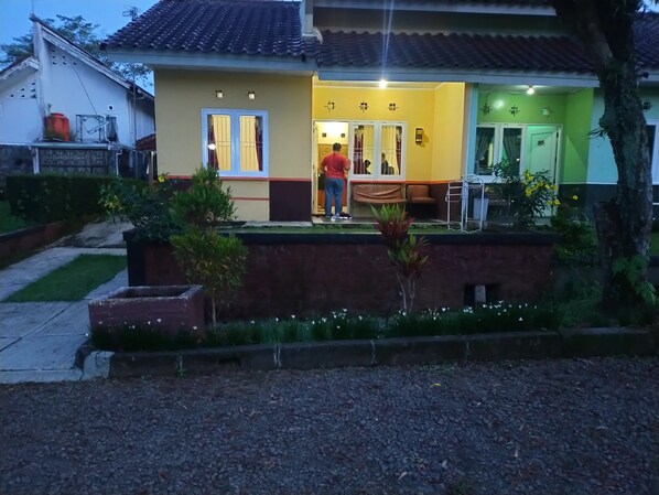 A residential house with a tiled roof, a front porch, and a small garden area with plants and a gravel pathway.