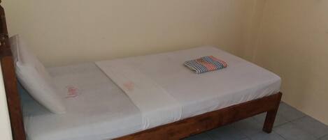 Una cama individual con estructura de madera, colchón blanco y una manta a rayas doblada.