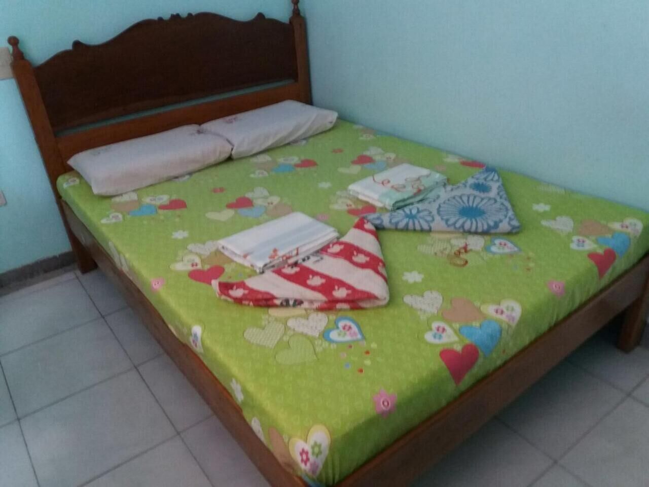 Un letto con una coperta a fiori verdi, due cuscini e un cuscino a righe rosse e bianche.