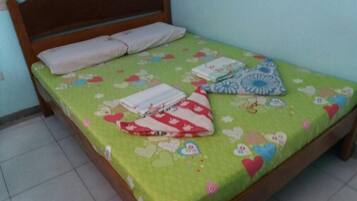 Un letto con una coperta a fiori verdi, due cuscini e un cuscino a righe rosse e bianche.