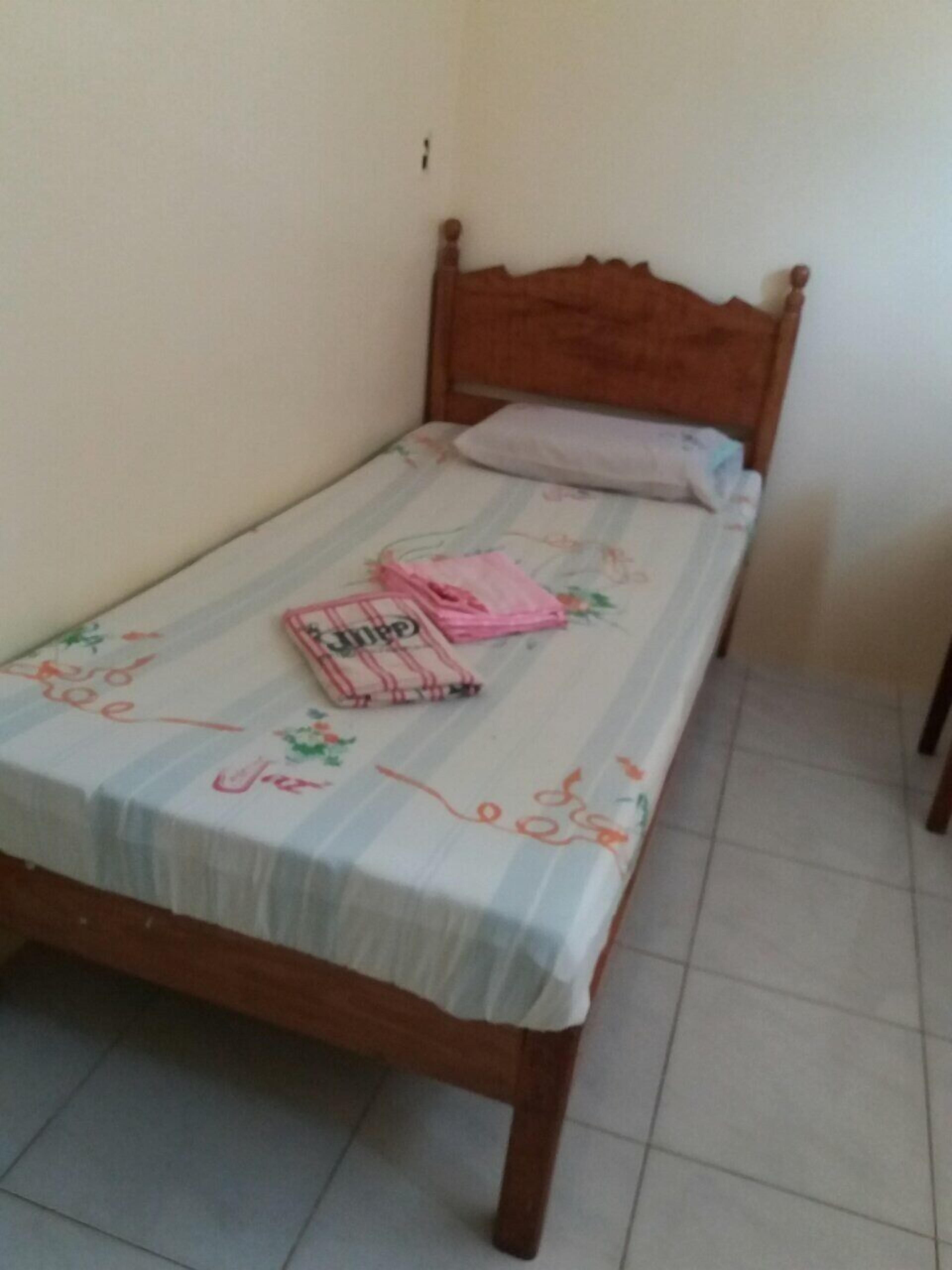 Una cama individual con cabecera de madera, colcha estampada con motivos florales y una manta rosa doblada sobre la cama.