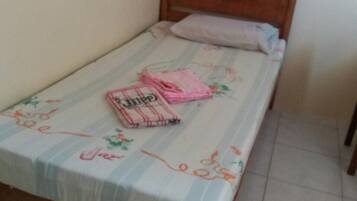 Una cama individual con cabecera de madera, colcha estampada con motivos florales y una manta rosa doblada sobre la cama.