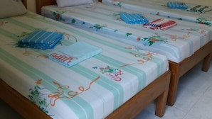 Een kamer met drie houten bedden, elk voorzien van beddengoed en kussens met een bloemendesign.