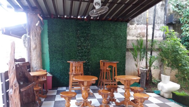 Een overdekt terras met houten tafels en stoelen, een groene wand en een geruite vloer.