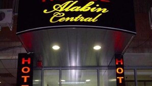 The exterior of a hotel with a neon sign reading "HOTEL Alabin Central" and the word "HOTEL" displayed on the glass doors. - Hotel Alabin Central (Sofia)